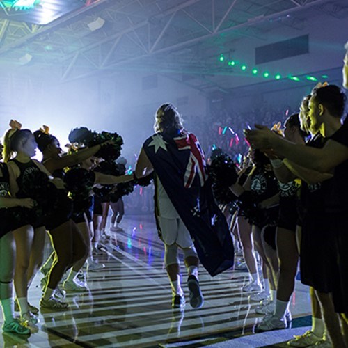 An athlete runs down a corridor of cheerleaders and teammates at a night time sports celebration event